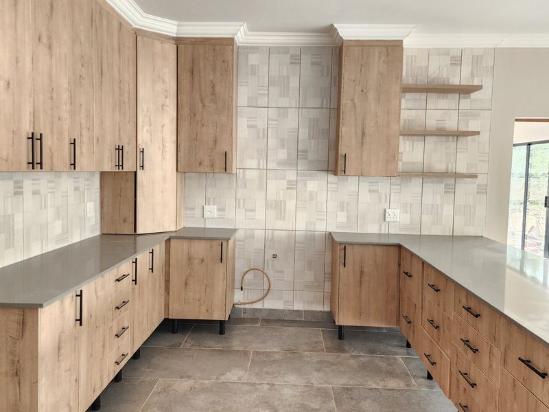 Modern kitchen featuring wood-look cabinetry, stone countertops, tiled backsplash, and floating shelves in a clean, contemporary layout.