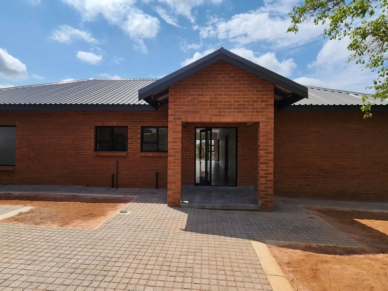 A modern face brick house exterior featuring a metal roof, aluminium window frames, and a paved entrance area with unfinished landscaping.