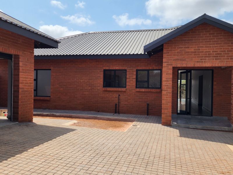 A modern face brick house exterior featuring a paved driveway, corrugated metal roofing, and aluminum window frames, with some landscaping still to be completed.