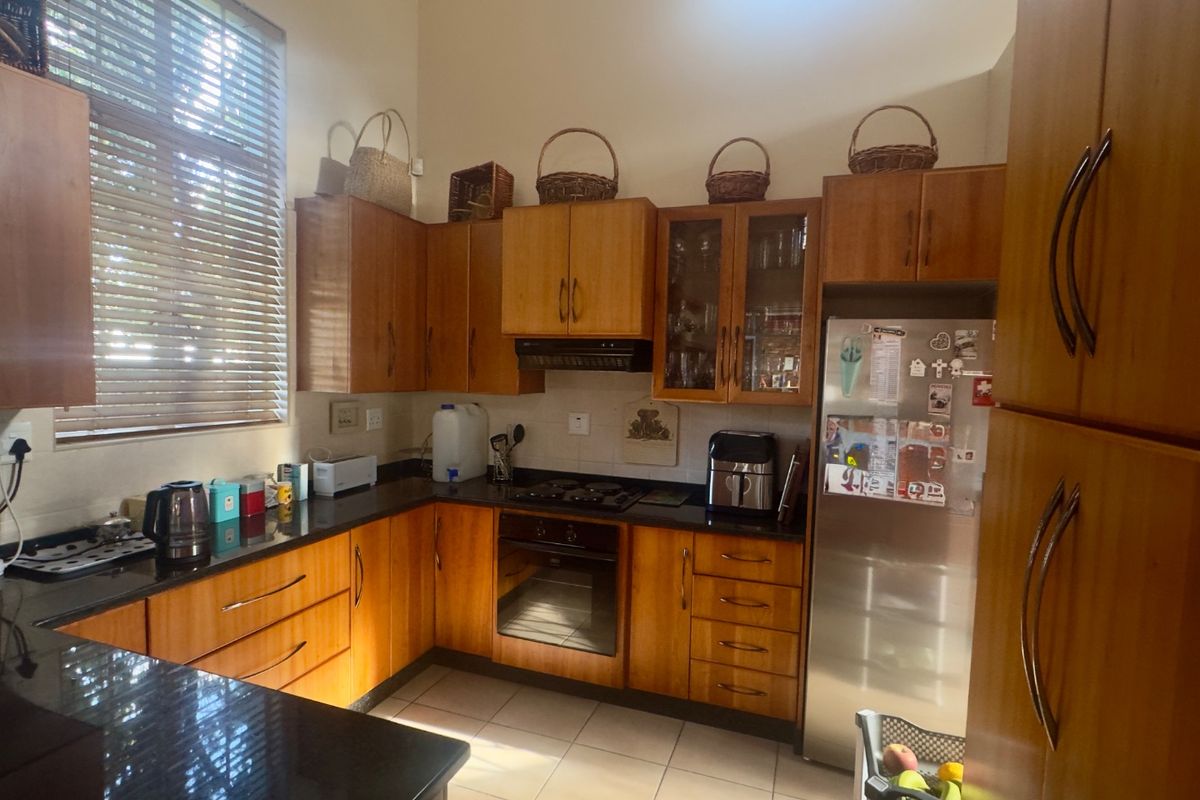 A functional kitchen featuring warm-toned wooden cabinetry, granite countertops, built-in oven, gas hob, and tiled flooring with ample natural light.
