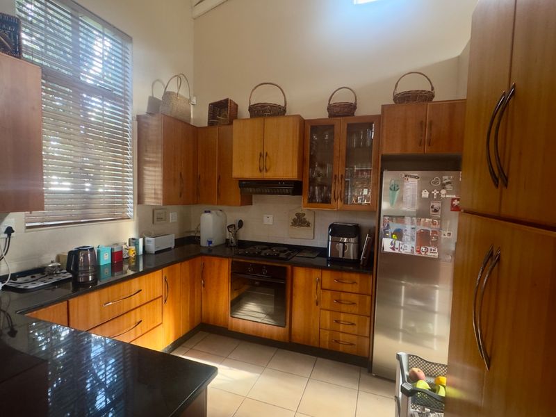 A functional kitchen featuring warm-toned wooden cabinetry, granite countertops, built-in oven, gas hob, and tiled flooring with ample natural light.