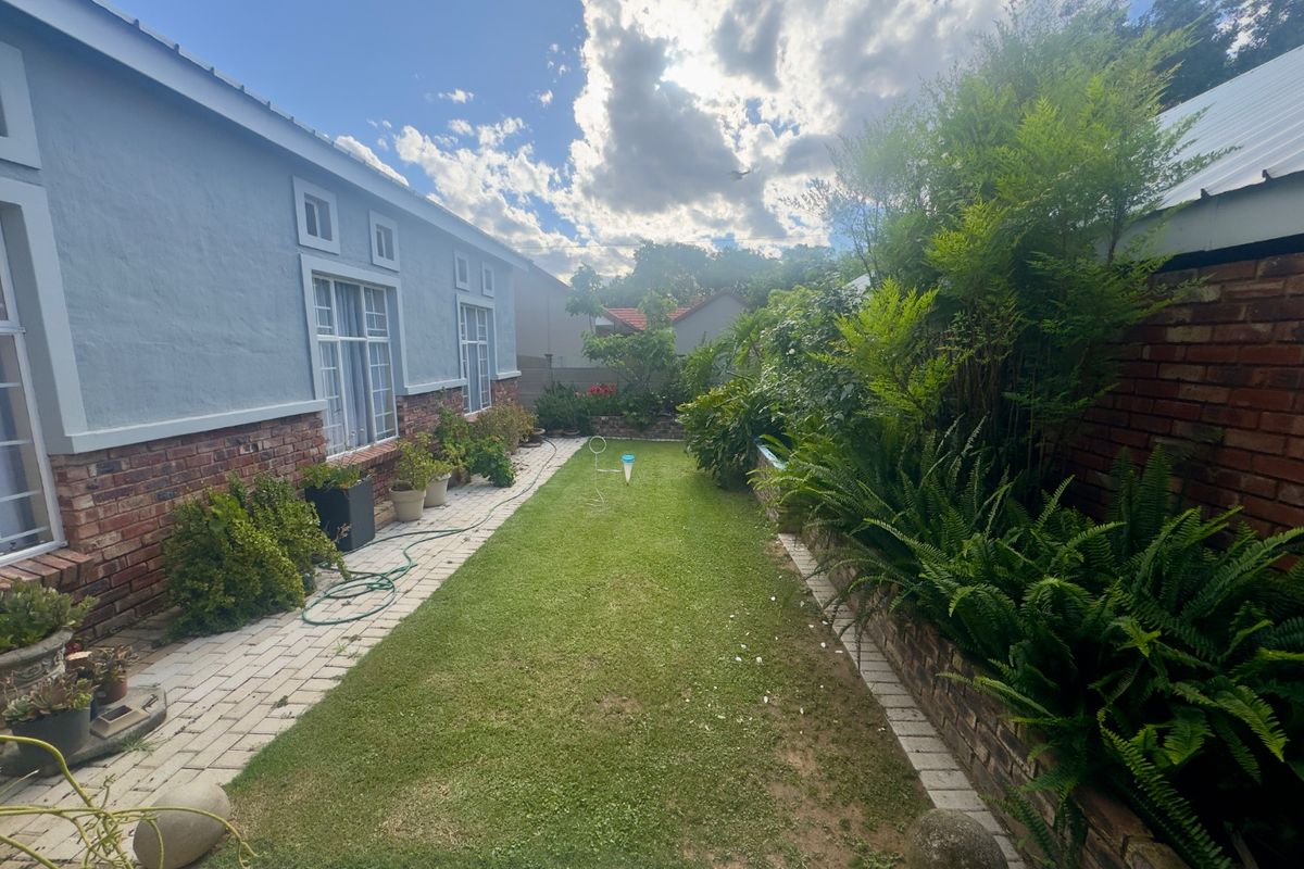 A well-maintained rear garden featuring a central lawn, paved pathway, and established perimeter landscaping alongside the brick and plaster townhouse exterior.