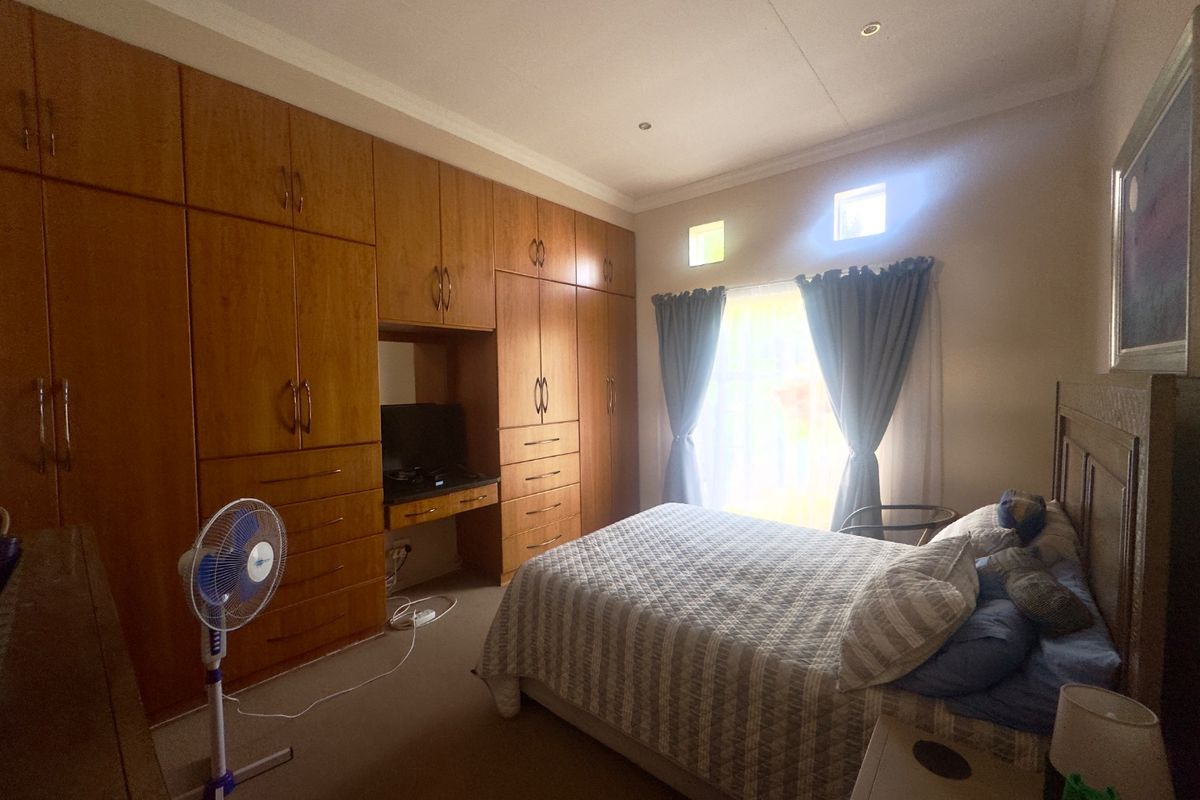 A bedroom featuring extensive wall-to-wall built-in wooden cabinetry with an integrated vanity desk, neutral carpeting, and natural light from a window with curtains.