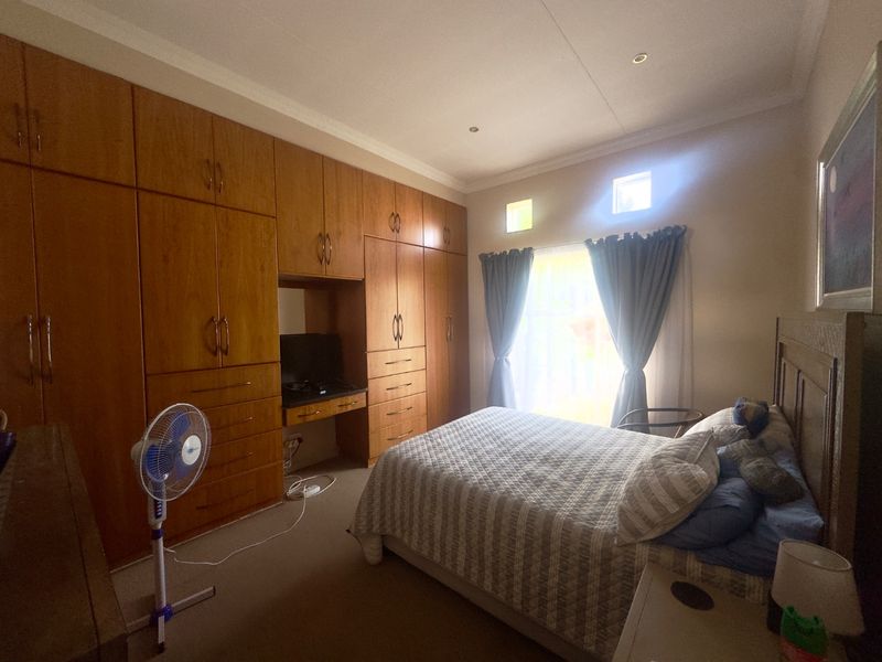 A bedroom featuring extensive wall-to-wall built-in wooden cabinetry with an integrated vanity desk, neutral carpeting, and natural light from a window with curtains.