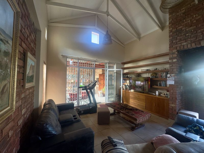 Spacious living room featuring a vaulted ceiling, exposed brick walls, and custom built-in wooden cabinetry with shelving, leading out to a covered patio area.