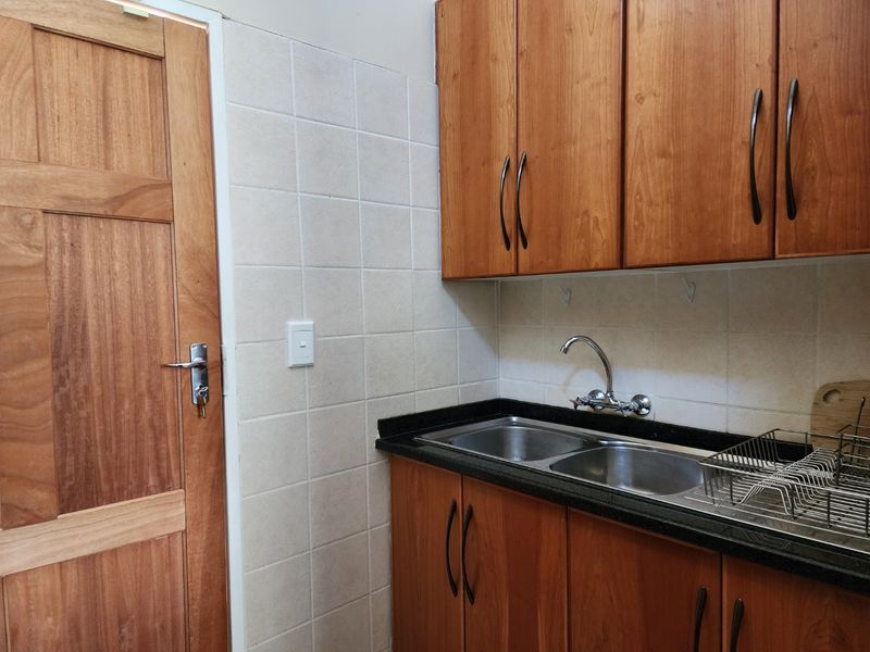 A functional scullery area featuring wooden cabinetry, a double bowl stainless steel sink, stone countertops, and a tiled splashback.