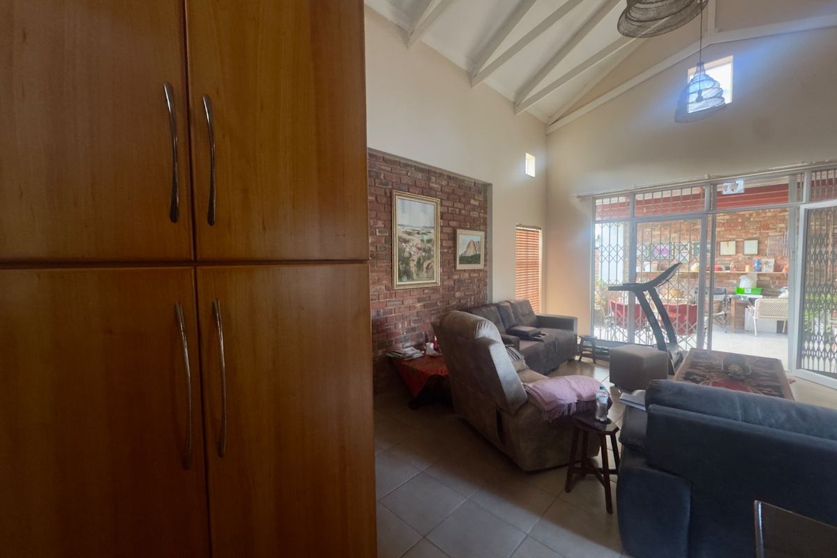 Spacious living area featuring a vaulted ceiling, exposed brick wall, tiled floors, and large sliding doors providing access to the outdoor patio.
