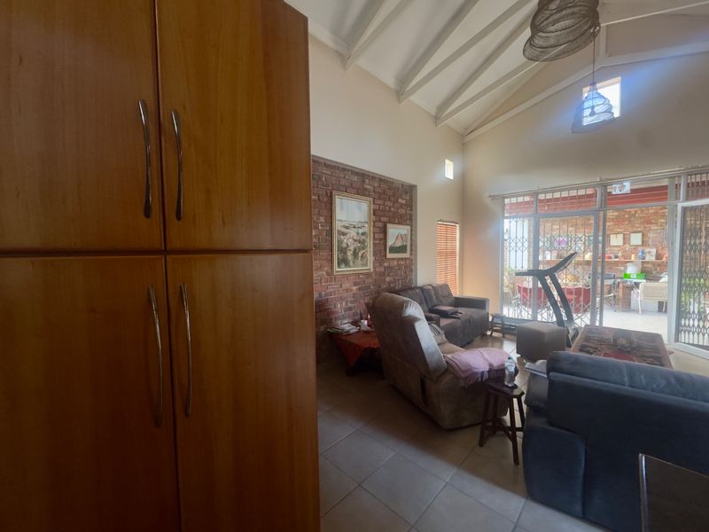 Spacious living area featuring a vaulted ceiling, exposed brick wall, tiled floors, and large sliding doors providing access to the outdoor patio.