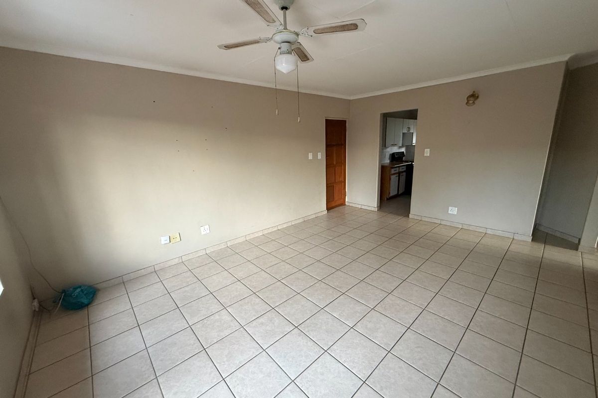 An empty living room featuring tiled flooring, a ceiling fan, and coved ceilings, with a view through to the kitchen area.