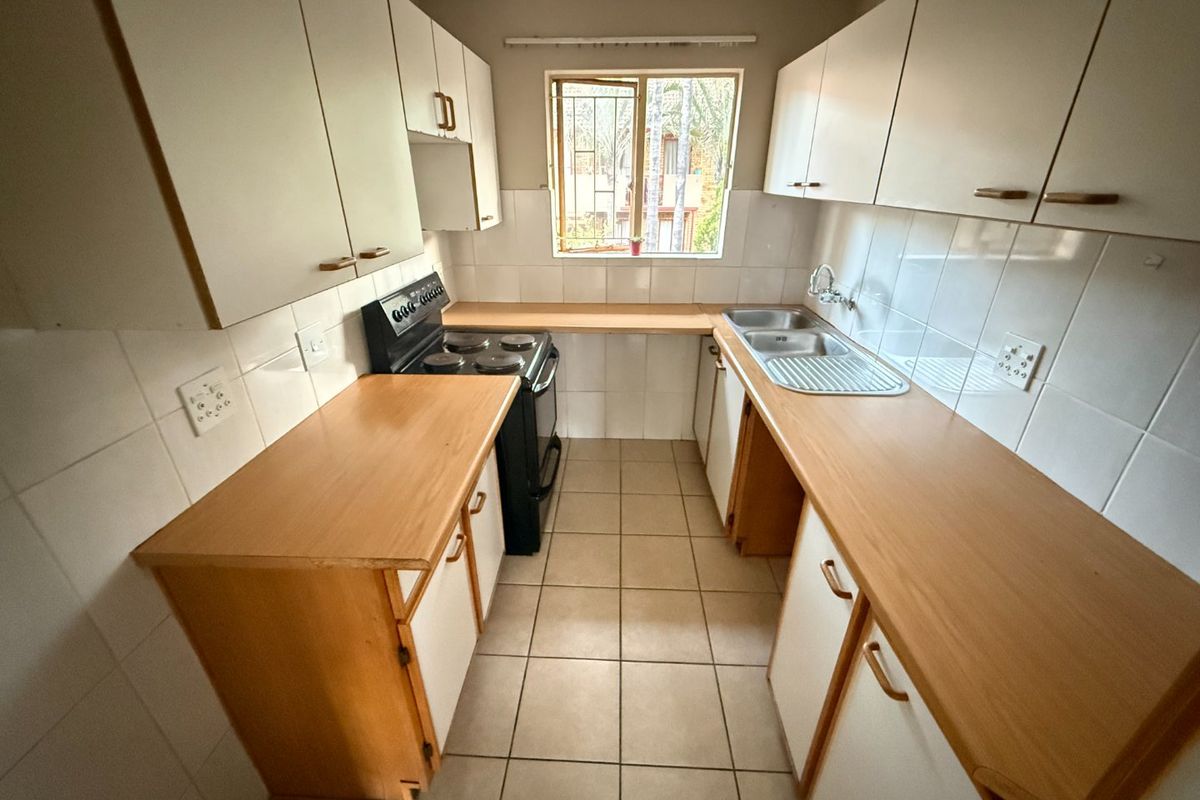 A functional galley-style kitchen featuring built-in cabinetry, laminate countertops, a double bowl sink, and a freestanding stove with tiled splashbacks.