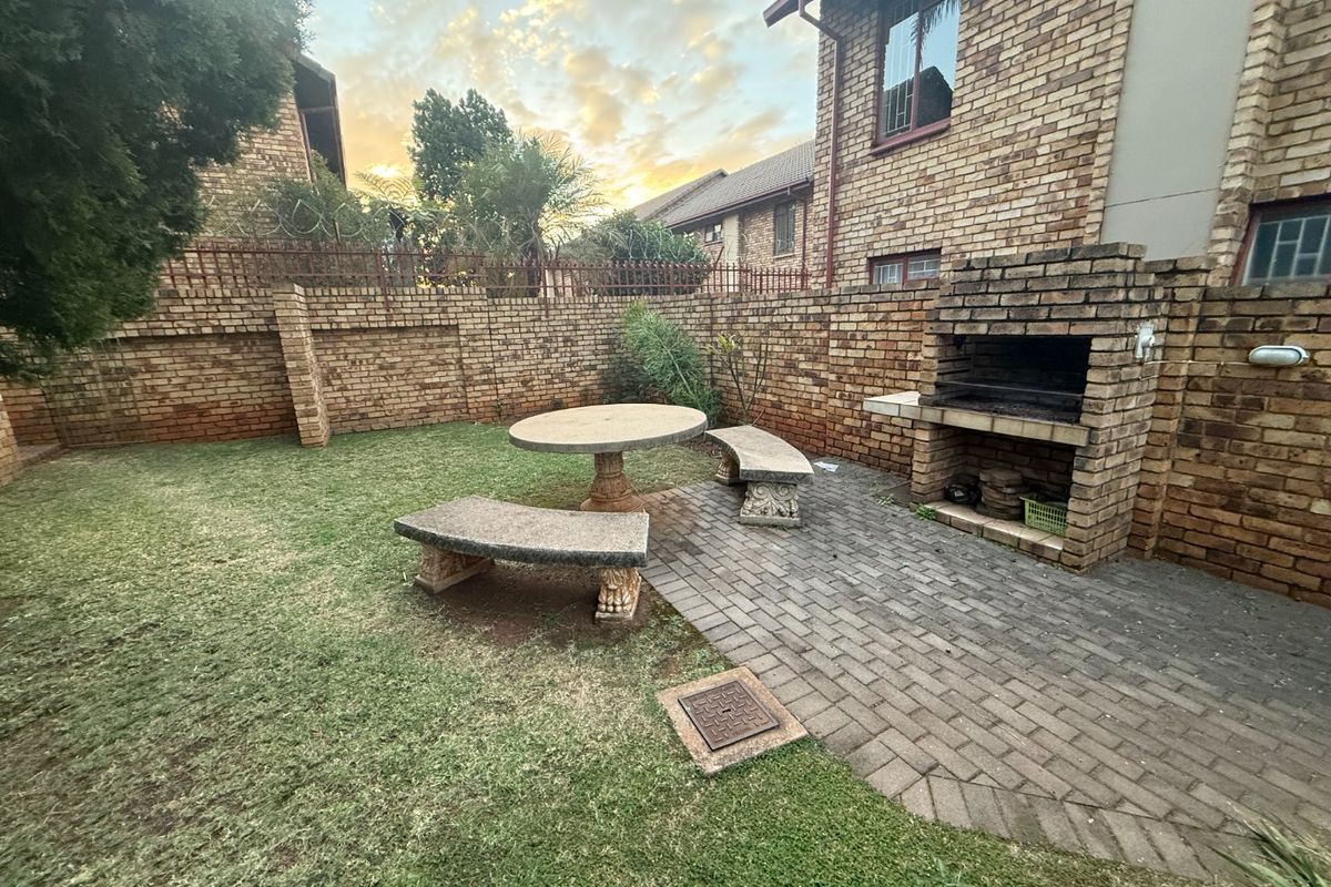 Private rear garden featuring a paved patio area with a built-in brick braai, enclosed by high brick boundary walls.