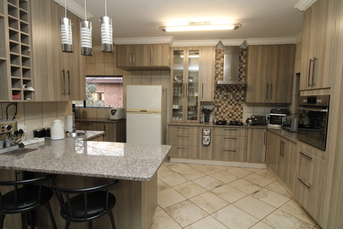 A well-appointed kitchen featuring wood-grain cabinetry, granite countertops, a gas hob with extractor, and a built-in oven, complemented by tiled flooring and mosaic backsplash.