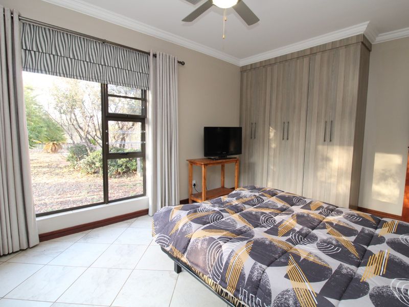 A well-maintained bedroom featuring built-in cupboards, tiled flooring, a ceiling fan, and a large window providing natural light and garden views.