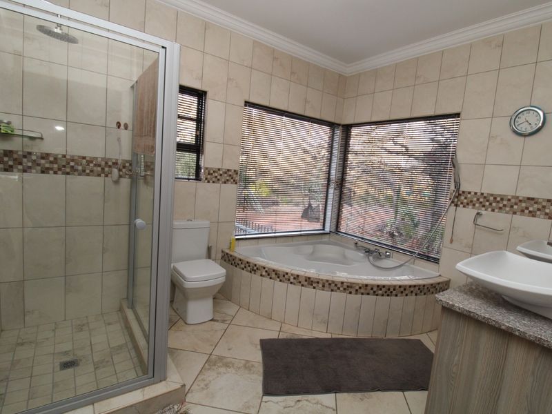 A functional bathroom featuring a corner bathtub, a separate glass-enclosed shower, a vanity with a basin, and neutral ceramic tiling throughout.
