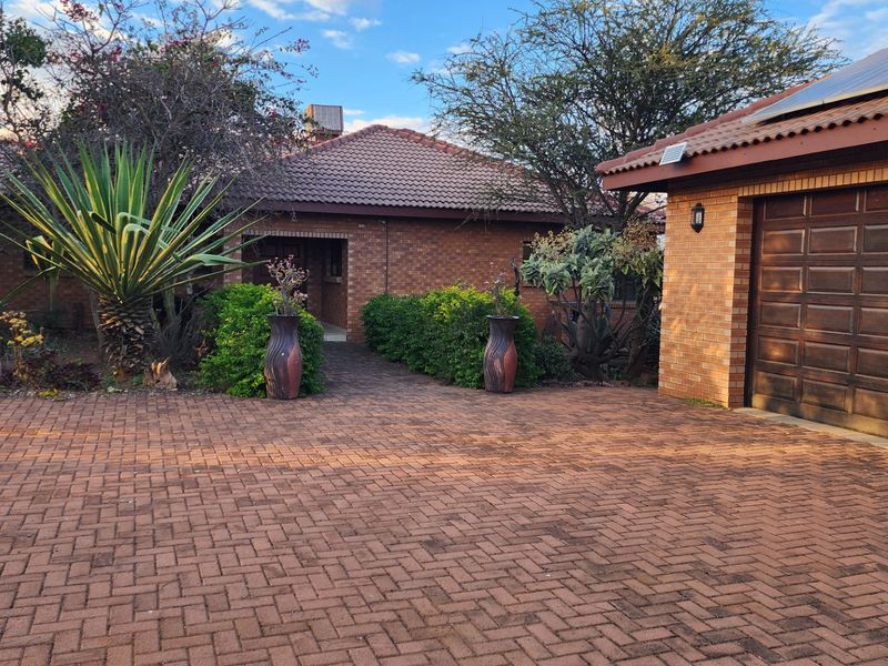 Front view of a brick house featuring a paved driveway, integrated garage, and established garden landscaping.