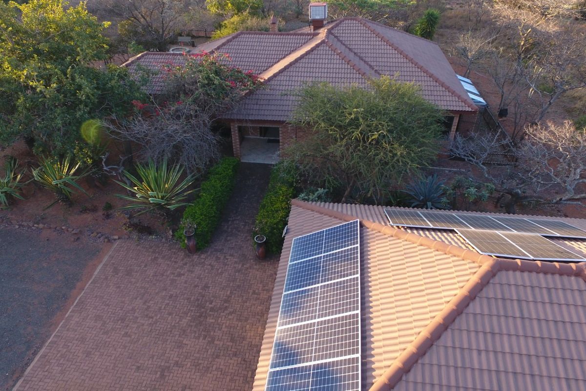 Aerial view of a residential property featuring a tiled roof with installed solar panels and a paved driveway entrance.