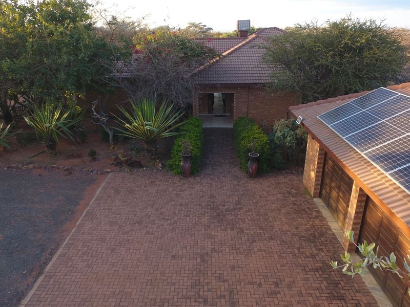 Aerial view of the front entrance featuring a paved driveway, brick facade, and solar panels installed on the garage roof.