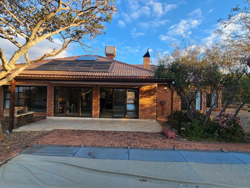 Rear view of a brick house featuring a covered patio, sliding glass doors, solar panels, and a swimming pool with a cover.