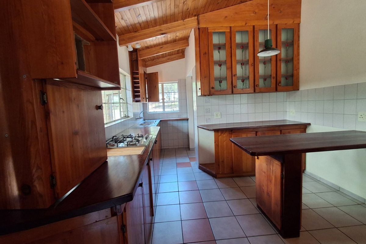 A spacious kitchen featuring extensive wooden cabinetry, a gas hob, tiled flooring, and a built-in breakfast counter under a vaulted wooden ceiling.