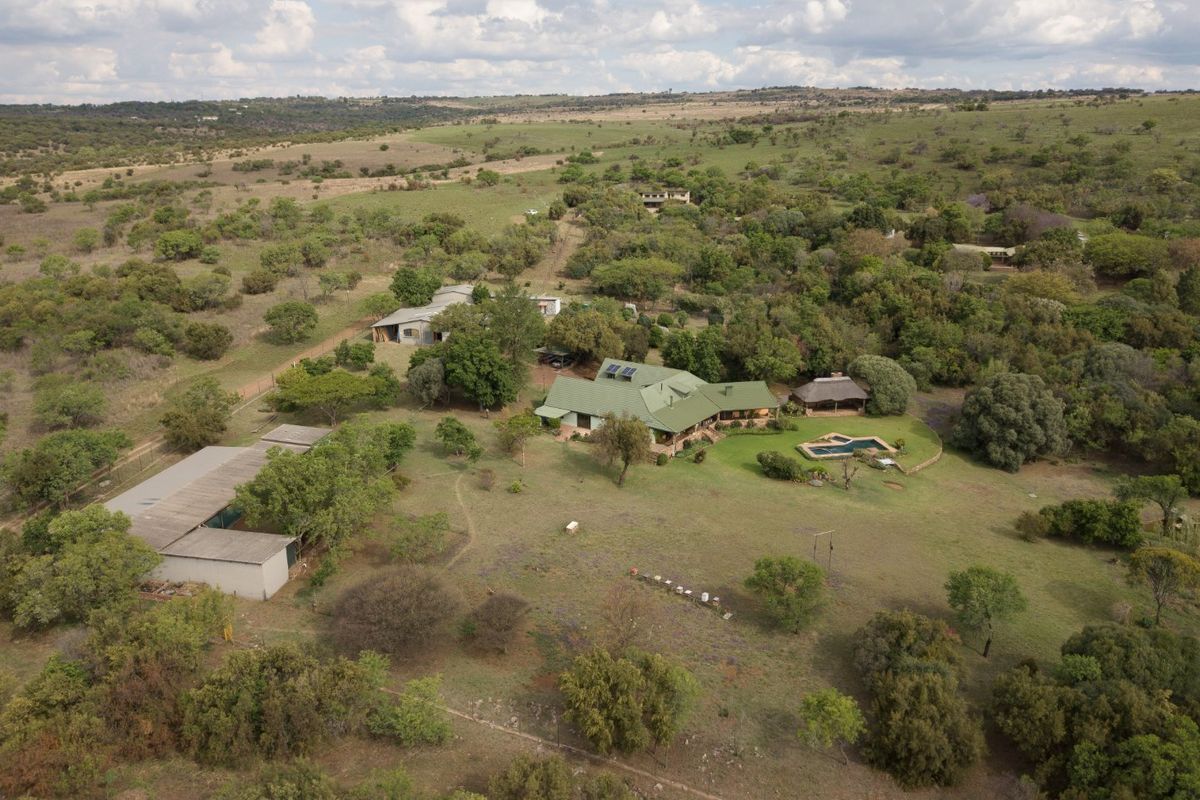 Aerial view of a large rural property featuring a main residence with solar panels, a swimming pool, a thatched gazebo, and multiple outbuildings.