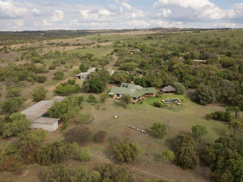 Aerial view of a large rural property featuring a main residence with solar panels, a swimming pool, a thatched gazebo, and multiple outbuildings.