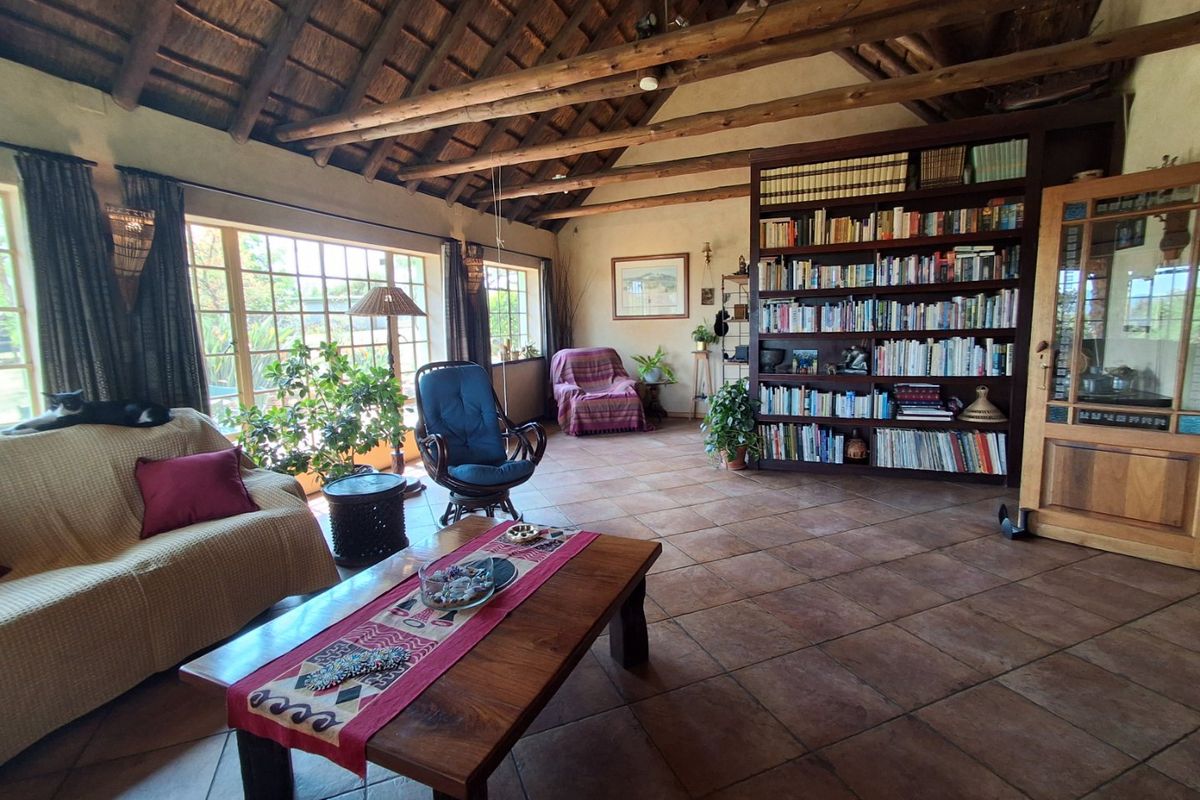 Spacious living room featuring a high thatched ceiling with exposed timber rafters, terracotta tiled flooring, and a large built-in wooden bookshelf.