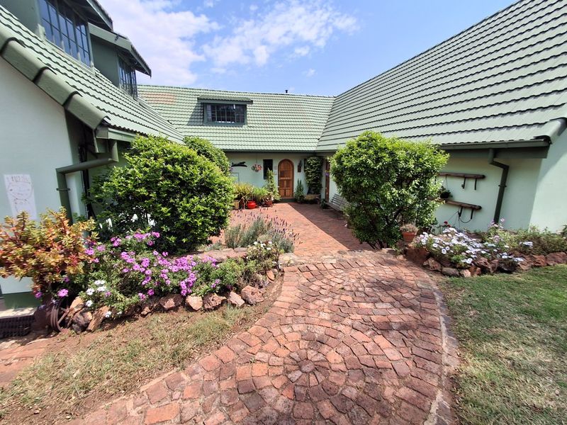 A charming rear courtyard featuring a brick-paved pathway, established garden beds with stone edging, and a classic arched wooden entrance door.