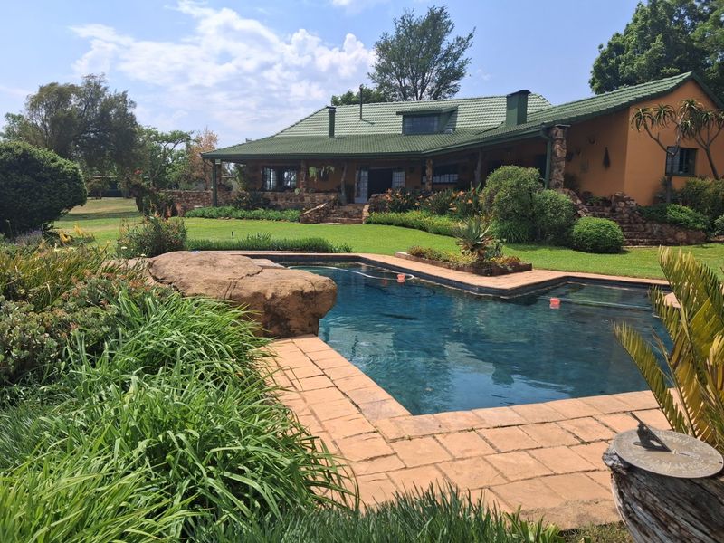 A well-maintained swimming pool area featuring natural stone accents, surrounded by a lush landscaped garden and a view of the main house exterior.