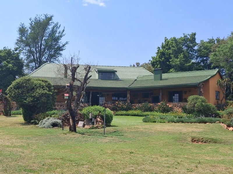 A charming single-story home featuring a green tiled roof, stone accents, and a spacious covered patio overlooking a well-maintained garden.