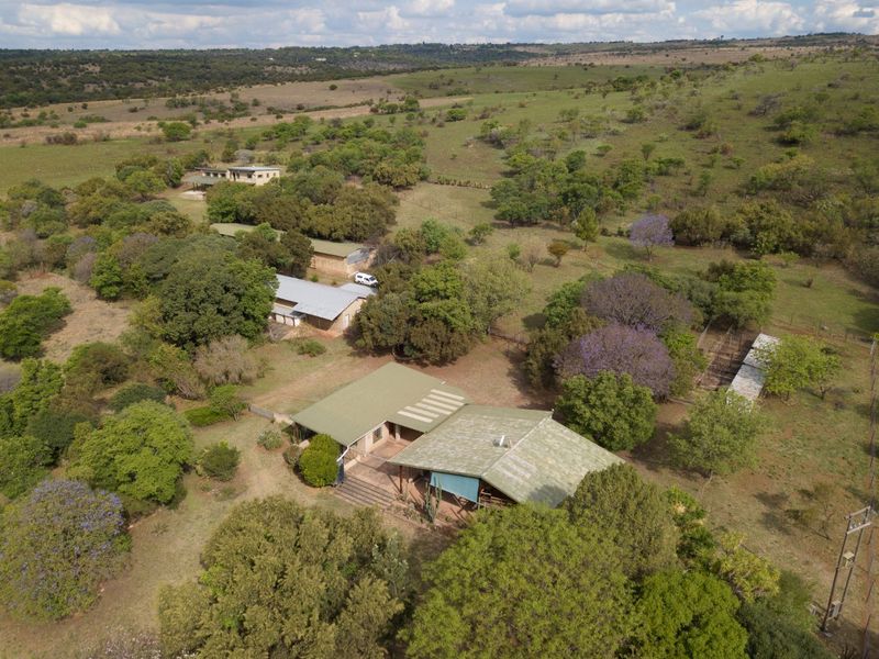 Aerial view of a rural property featuring a main residence with a metal roof, covered patio, and multiple outbuildings set within a large landscape.