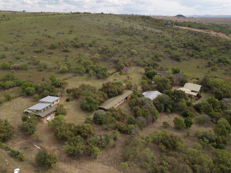 Aerial view of a rural property featuring multiple detached structures set within a large, natural landscape with established trees and fencing.
