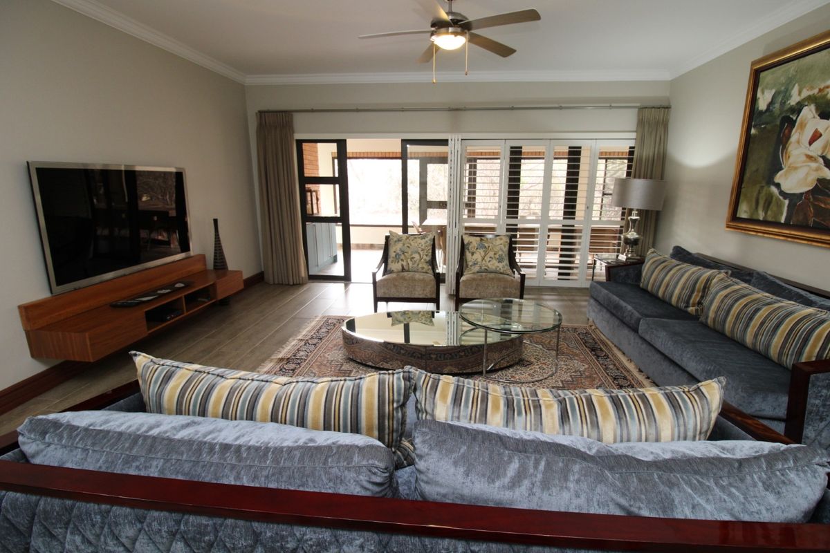Spacious living room featuring tiled flooring, crown molding, a ceiling fan, and large sliding glass doors with plantation shutters leading to an outdoor area.