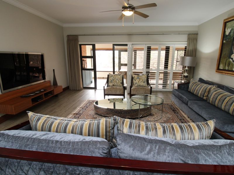 Spacious living room featuring tiled flooring, crown molding, a ceiling fan, and large sliding glass doors with plantation shutters leading to an outdoor area.