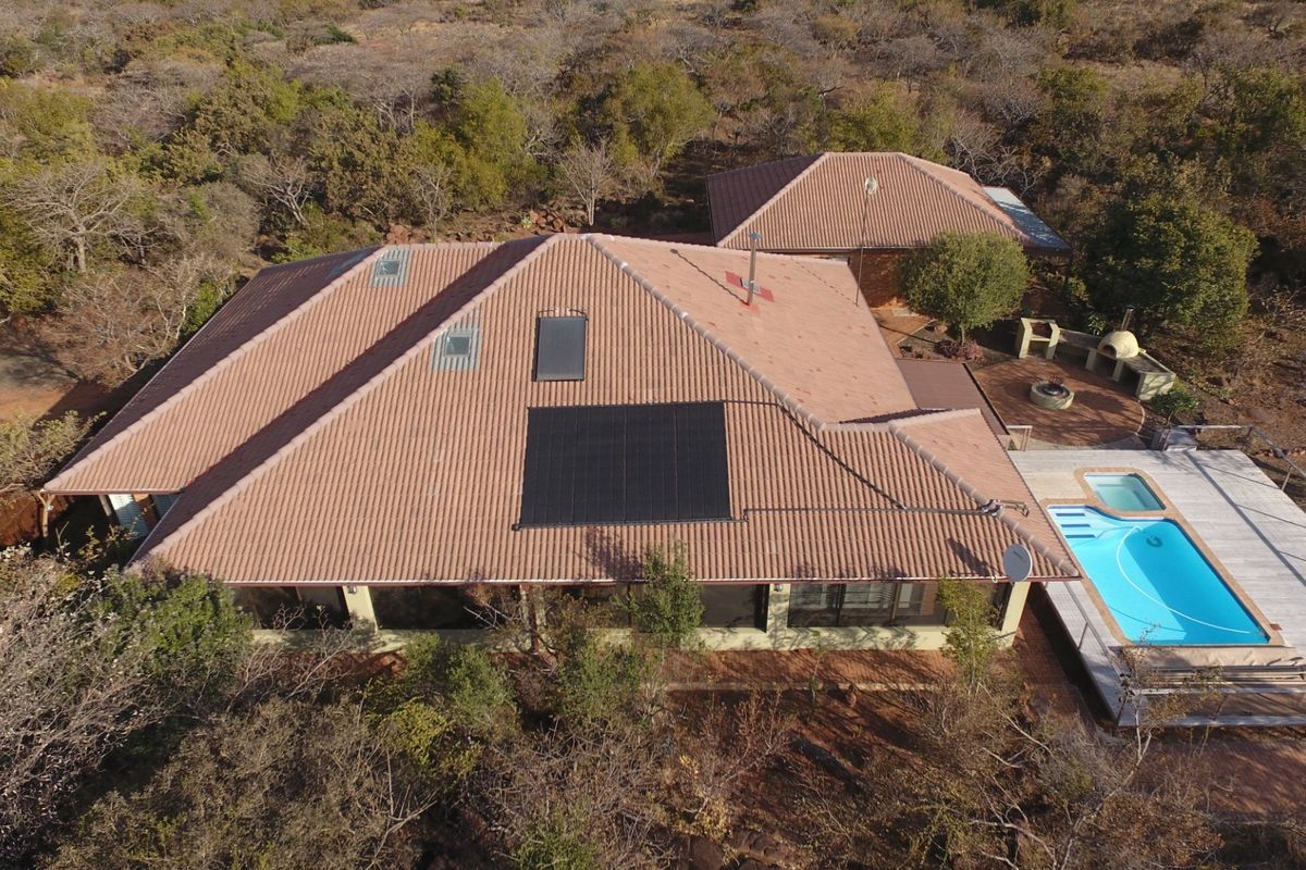 Aerial view of a residential property featuring a tiled roof with solar panels, a swimming pool, and an outdoor entertainment area set in natural surroundings.