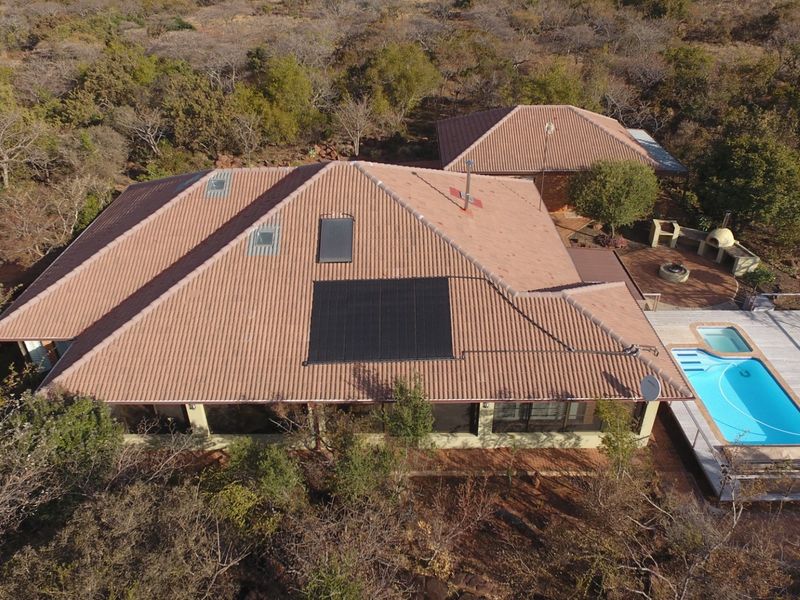 Aerial view of a residential property featuring a tiled roof with solar panels, a swimming pool, and an outdoor entertainment area set in natural surroundings.