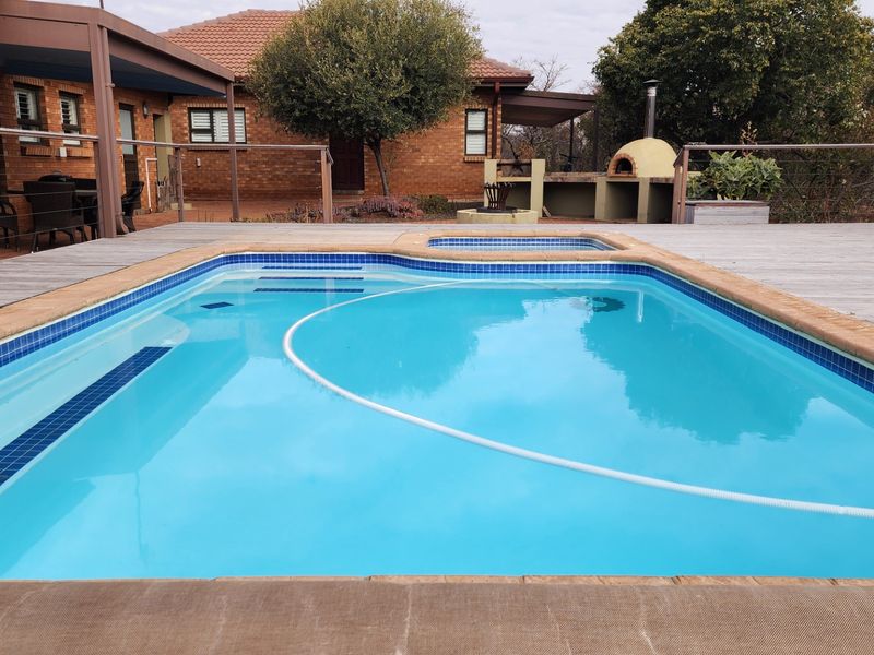 Outdoor entertainment area featuring a swimming pool with integrated spa, timber decking, and a built-in pizza oven set against a brick house exterior.
