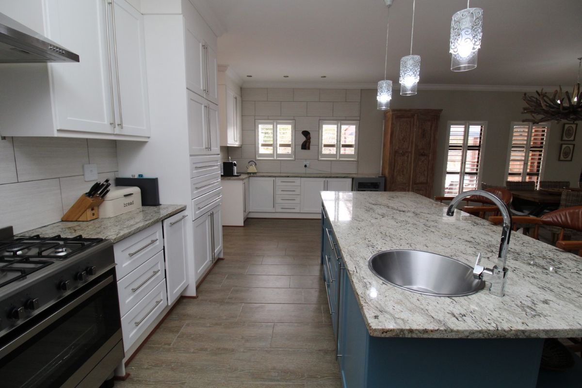 Modern kitchen featuring a large granite-topped island with an integrated sink, gas stove, ample cabinetry, and stylish pendant lighting.
