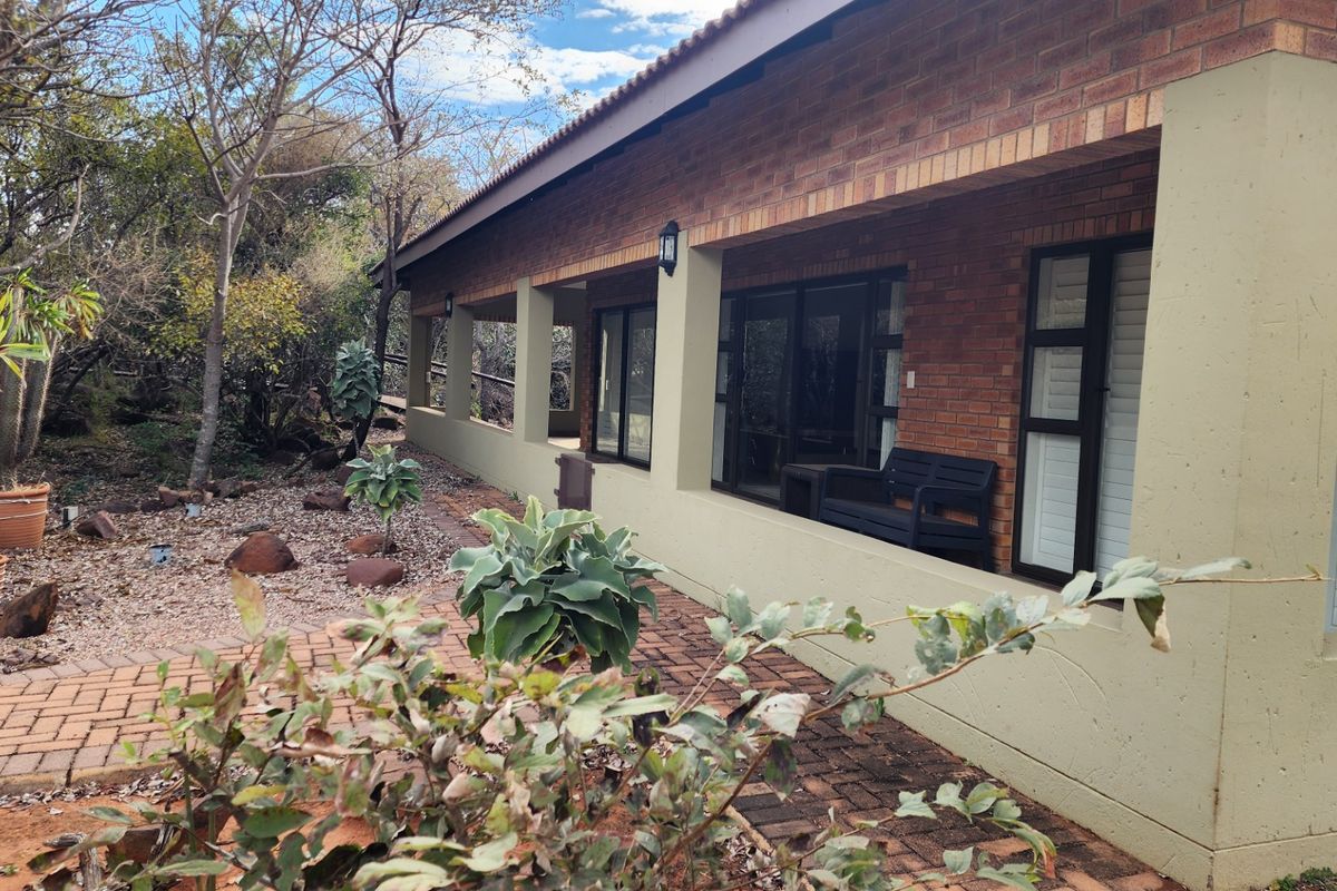 A rear view of the house featuring a covered patio with brick facade, sliding glass doors, and a paved walkway leading through the garden.
