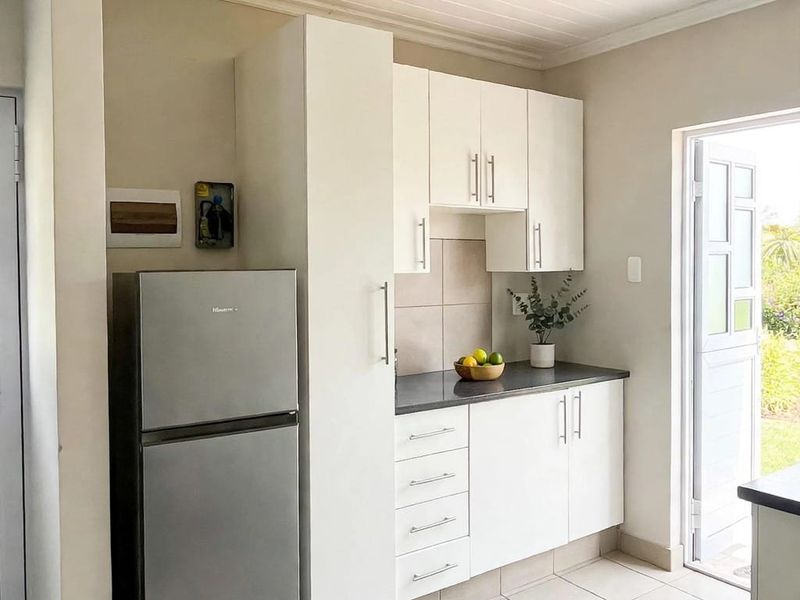 A compact, well-maintained kitchen featuring white cabinetry, dark countertops, tiled backsplash, and direct access to the outdoor area.