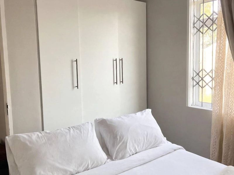 A clean and well-maintained bedroom featuring a modern white built-in wardrobe and a window fitted with a security gate.
