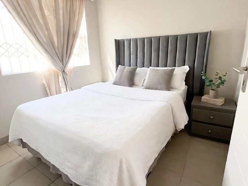 A well-maintained bedroom featuring neutral wall tones, tiled flooring, and a window fitted with security bars.