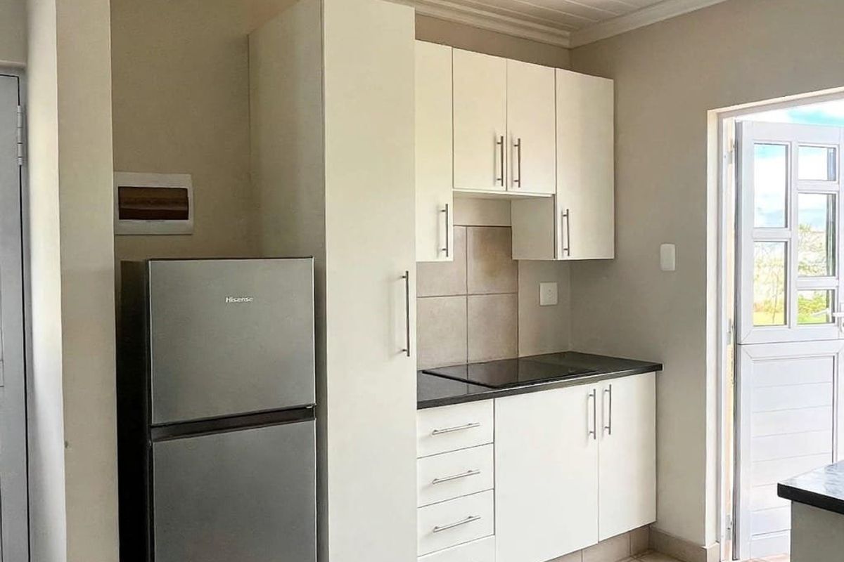 A compact kitchen featuring white built-in cabinetry, a black hob, tiled backsplash, and tiled flooring with direct access to an outdoor area.
