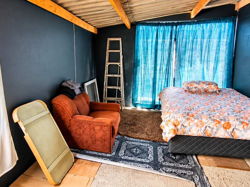 A bedroom featuring exposed timber rafters and dark painted blockwork walls, offering a rustic aesthetic with potential for modern interior finishing.