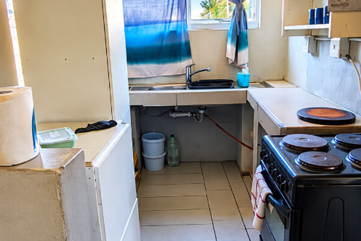 A functional kitchen area featuring tiled flooring, a stainless steel sink, and an electric stove, requiring cosmetic updates to improve its overall condition.