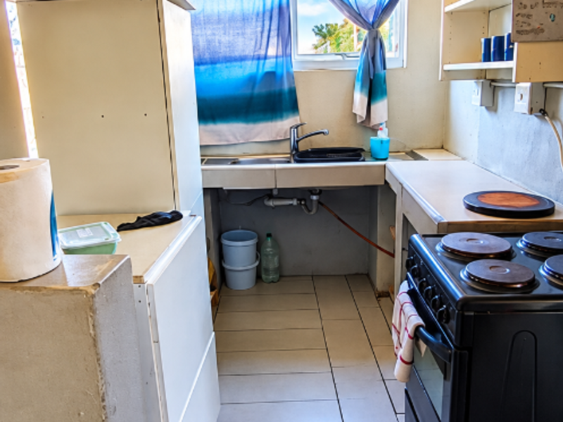 A functional kitchen area featuring tiled flooring, a stainless steel sink, and an electric stove, requiring cosmetic updates to improve its overall condition.
