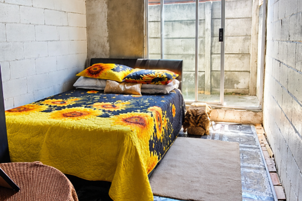 A bedroom featuring exposed concrete block walls, a timber-clad ceiling, and patterned floor tiles, with direct access to an outdoor area via sliding glass doors.