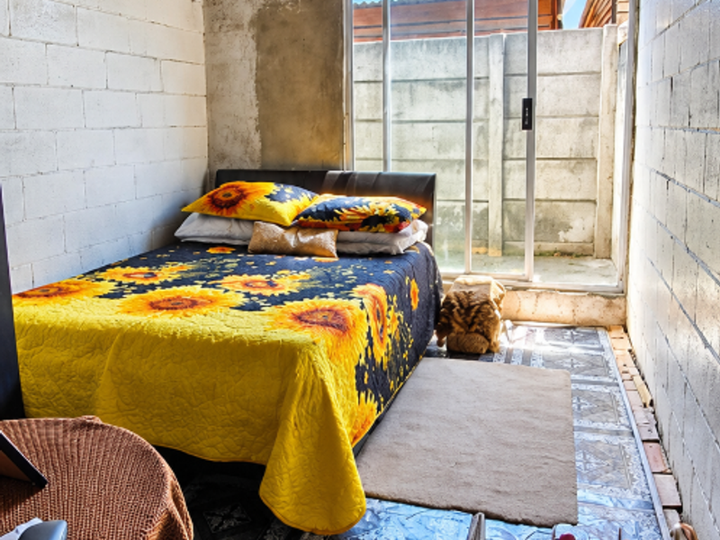 A bedroom featuring exposed concrete block walls, a timber-clad ceiling, and patterned floor tiles, with direct access to an outdoor area via sliding glass doors.