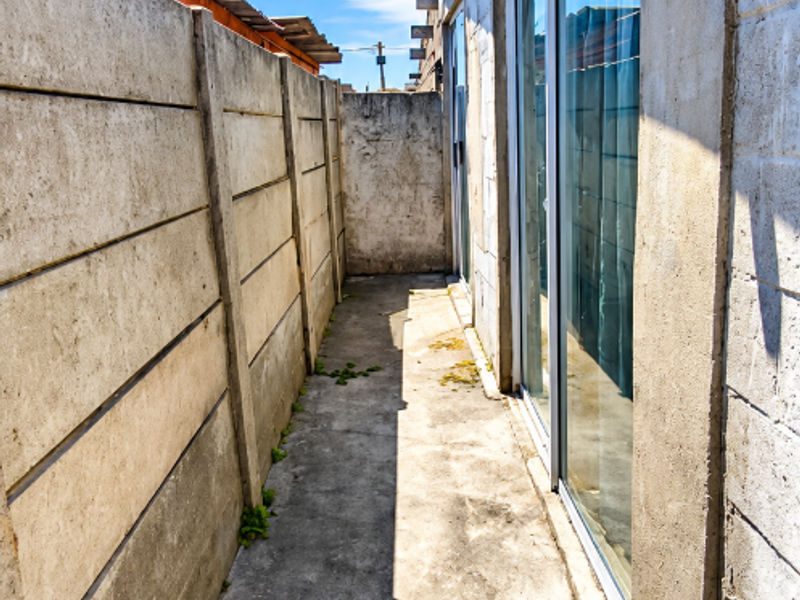 A narrow side passage featuring a concrete pathway, boundary wall, and sliding glass door access to the property.