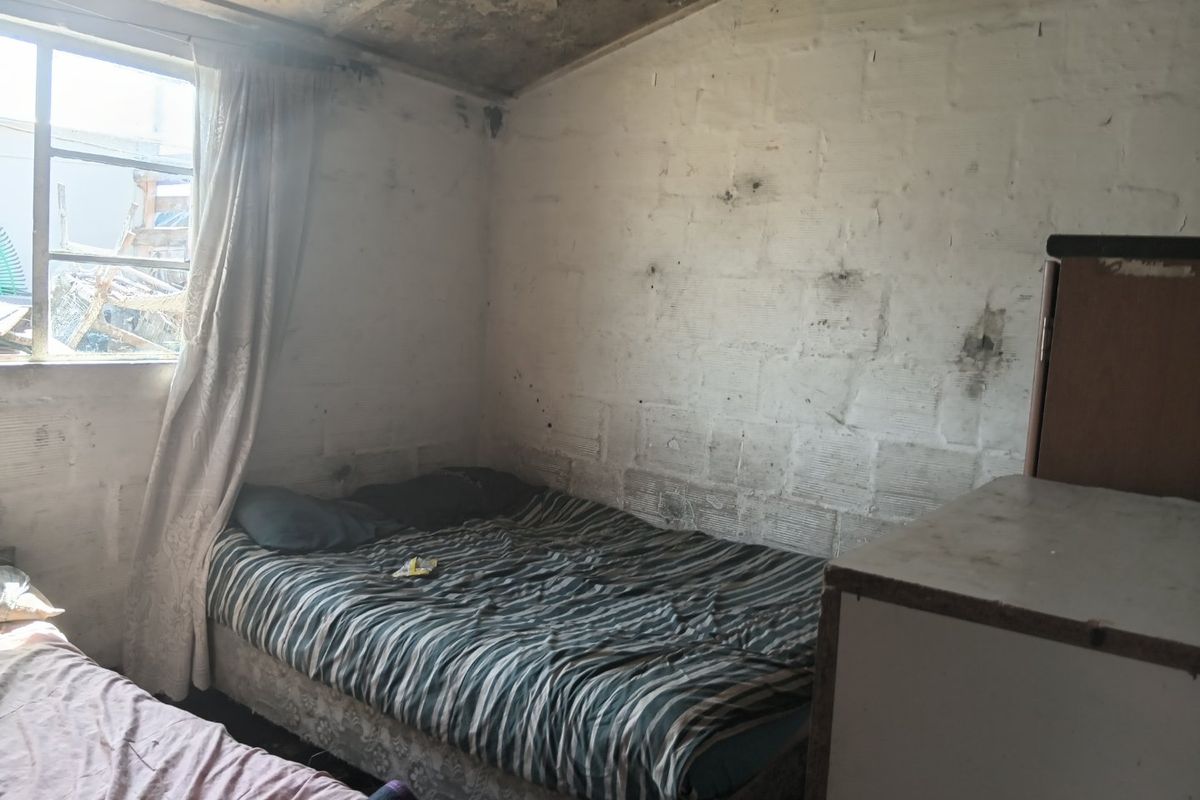 A bedroom featuring exposed concrete block walls and a concrete ceiling, requiring significant renovation and surface finishing to improve habitability.