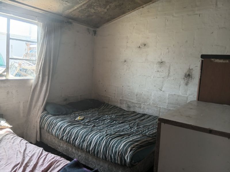 A bedroom featuring exposed concrete block walls and a concrete ceiling, requiring significant renovation and surface finishing to improve habitability.